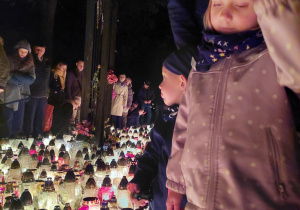Dziewczynka stojąca na tle zniczy zapalonych w miejscu pamięci
