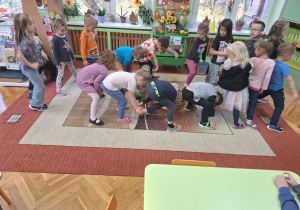 Na zdjęciu stoją dzieci i podają sobie dołem dynie z rąk do rąk.