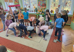 Na zdjęciu stoją dzieci i podają sobie dołem dynie z rąk do rąk.