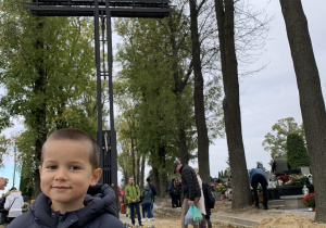Chłopiec stoi w miejscu pamięci zasłużonych Polaków na cmentarzu na Dołach.