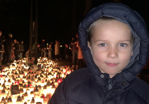Chłopiec stoi w miejscu pamięci zasłużonych Polaków na cmentarzu na Dołach.