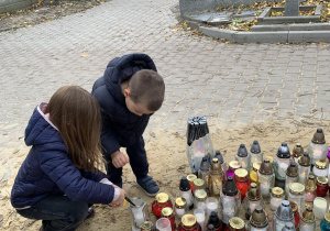 Chłopiec z dziewczynka zapalają znicze w miejscu pamięci zasłużonych Polaków na cmentarzu na Dołach.