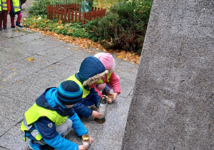 na zdjęciu troje dzieci stawia zapalone znicze pod pomnikiem G. Narutowicza
