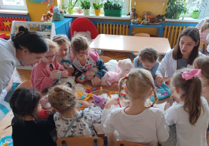 -na zdjęciach dzieci przy przedszkolnych stolikach bawią się wraz ze studentami medycyny w lekarzy i pacjentów. wykorzystują do tego zabawki - pluszaki przyniesione przez dzieci oraz zabawkowy i prawdziwy sprzęt medyczny: plasterki, bandaże, strzykawki, stetoskopy, a także oglądają zdjęcia rtg. i podają na niby syropki