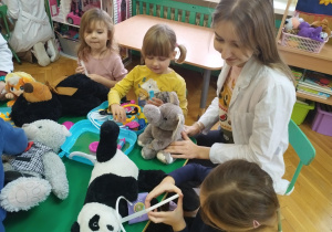 Dzieci siedzące przy stolikach wykonują przykładowe zabiegi lekarskie na swoich pluszakach