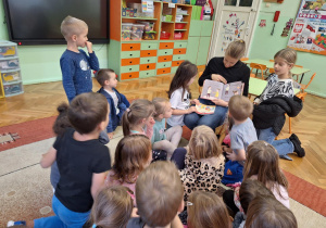 Mama Julci czyta bajkę dzieciom siedzącym na dywanie i pokazuje ilustracje w niej zawarte.