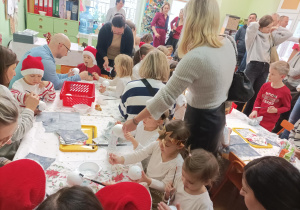 Na zdjęciu dzieci wraz z rodzicami ozdabiają styropianowe bombki.