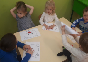 Zdjęcie przedstawia dzieci siedzące przy stolikach w trakcie realizacji pracy plastycznej "Mój miś” – etap pierwszy - wyklejanie elementów szablonu plasteliną