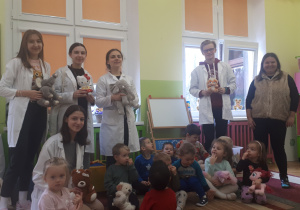 zdjęcie przedstawia dzieci z grupy ,,Misie’’ siedzące w klasie na dywanie wraz z studentami z Uniwersytetu Łódzkiego i Nauczycielką