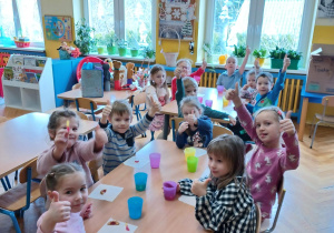 dzieci siedzą przy stolikach , jedzą ciasteczka i piją soczek