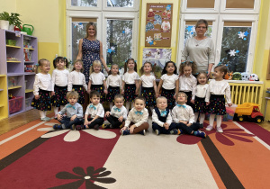 Na zdjęciu grupa dzieci wraz z nauczycielkami w odświętnych ubraniach przed występem z okazji Dnia Babci i Dziadka.