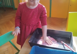 Dziewczynka zanurzająca dłoń w różowej farbie