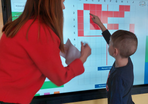 Dziecko stoi przed monitorem interaktywnym i patrzy na dyktando graficzne przedstawiające serce