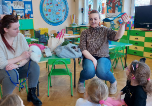 Kobieta z fundacji pokazuje dzieciom akcesoria potrzebne do pielęgnacji kotów.