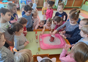 Dzieci oglądają i dotykają pianę wypływającą z wulkanu.