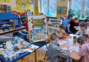 dzieci przy stolikach wypełniają kartę pracy - kolorują obrazki produktów ekologicznych