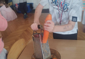 Chłopiec ścierający marchewkę na tarce.
