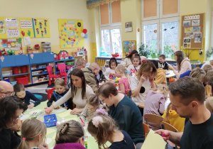 Dzieci wraz z rodzicami podczas wykonywania papierowych ozdób świątecznych.