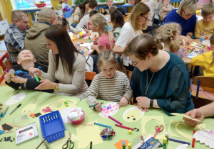Dzieci wraz z rodzicami podczas wykonywania papierowych ozdób świątecznych.