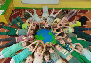 dzieci prezentują leżąc na podłodze wspólnie wykonaną pracę plastyczną