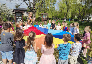 dzieci i nauczycielka podczas zabaw z chustą animacyjną w przyrodniczym zakątku