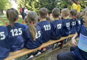 dzieci siedzące tyłem na ławce eksponujące numer 125