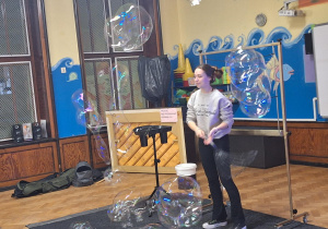 Na zdjęciu Pani za pomocą specjalnego sprzętu tworzy gigantyczne bańki mydlane.