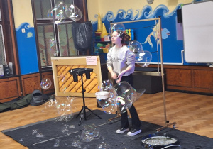 Na zdjęciu Pani za pomocą specjalnego sprzętu tworzy gigantyczne bańki mydlane.