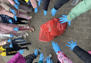 ręce dzieci w rękawiczkach oraz czerwony worek pełen znalezionych śmieci