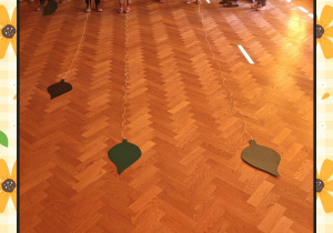 Na zdjęciu dzieci zawijają na patyk sznurek na końcu którego przyczepiony jest zielony liść.