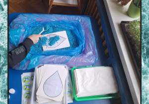 Na zdjęciu dziecko wykleja niebieskim ryżem szablon kropelki.