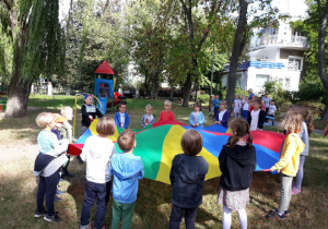 Dzieci z grupy piątej podczas zabawy w ogrodzie kolorową chustą