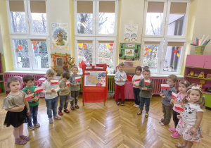 zdjęcie przedstawia dzieci z grupy II z flagami Polski stojące przy kąciku patriotycznym.