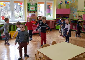 Zdjęcie przedstawia dzieci w trakcie zabawy ruchowej, naśladujące ruch wiatraka.