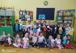 zdjęcie przedstawia grupę przedszkolaków w sali prezentujących prace plastyczne w kształcie kolorowych kredek