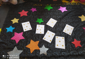 Zdjęcie przedstawia kolorowe gwiazdy oraz białe koperty z wróżbami na czarnym tle