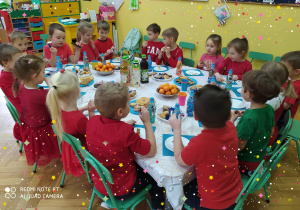 Dzieci z grupy pszczółek siedzą wokół stołu na którym znajdują się świąteczne smakołyki