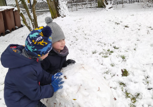 zdjęcie przedstawia dwóch chłopców turlających dużą śniegową kulę