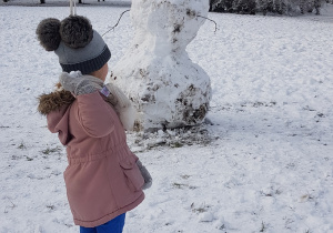 Zdjęcie przedstawia dziewczynkę celującą śnieżką w śniegowego bałwana.
