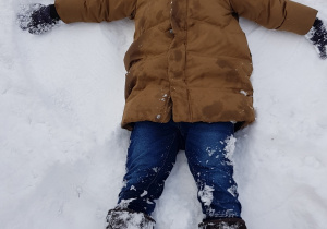 Zdjęcie przedstawia chłopca robiącego aniołka na śniegu.