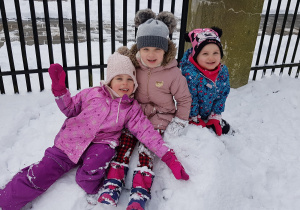 Zdjęcie przedstawia trzy dziewczynki siedzące na śniegu.