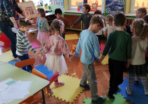 na zdjęciu - widok klasy przedszkolnej i tańczące dzieci w kole z nauczycielką