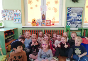 .na zdjęciu - dzieci siedzą na podłodze pod oknem, w tle na oknie, dekoracja poświęcona z Kubusiowi Puchatkowi, książeczki oraz małe pluszaki z bajki o Kubusiu Puchatki