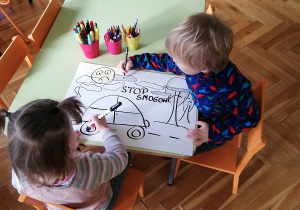Na zdjęciu widać dwoje dzieci siedzących przy stoliku i robiących plakat.