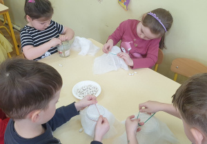 Zdjęcie przedstawia dzieci przygotowujące słoiczki do hodowli fasolek.