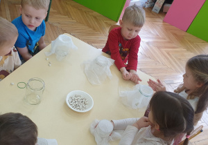 Zdjęcie przedstawia dzieci siedzące przy stoliku, przygotowujące się do zajęć