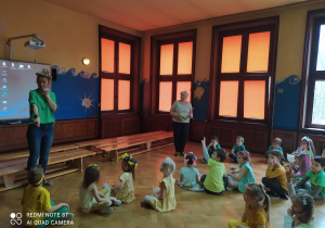 przedszkolaki siedzą na podłodze i odpowiadają na pytania zadawane przez nauczycielki