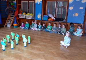 Dzieci siedzą na podłodze, przed nimi kręgle zrobione z butelek plastikowych ozdobionych na żabki