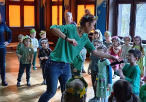 Dzieci w kole tańczą, jedno z nich śpiewa do mikrofony podanego przez nauczycielkę