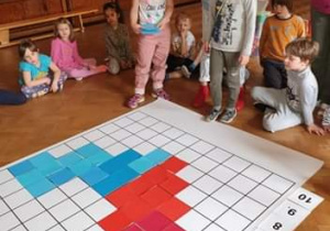 Dzieci układają na macie do kodowania serce z czerwonych i niebieskich kwadratów dla mamy i taty.
